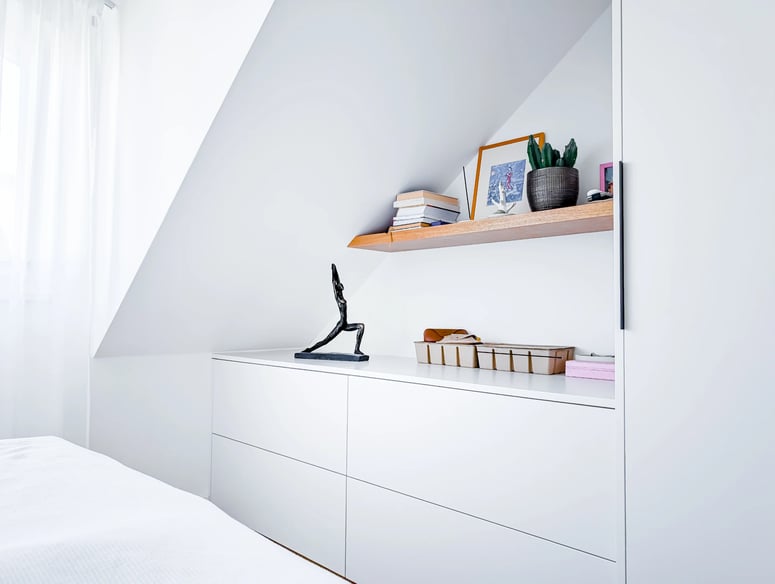 Bílý interiér s úložným prostorem a dřevěnou poličkou.